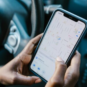 Close-up of hands holding a smartphone with GPS navigation displayed, in a car setting.